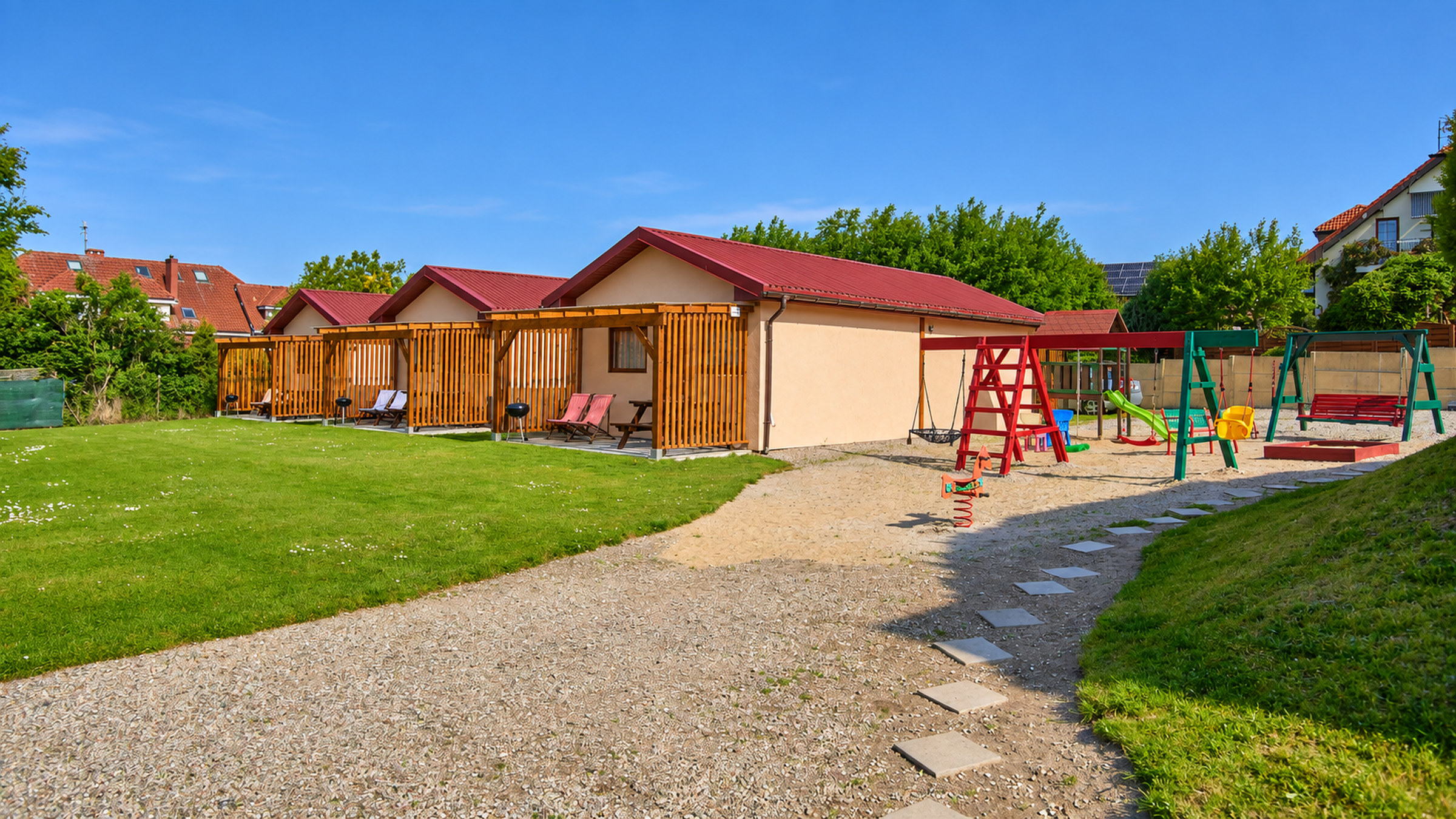 Drewniane domki z tarasami, zielony trawnik i plac zabaw w ogrodzie Domków u Agi
